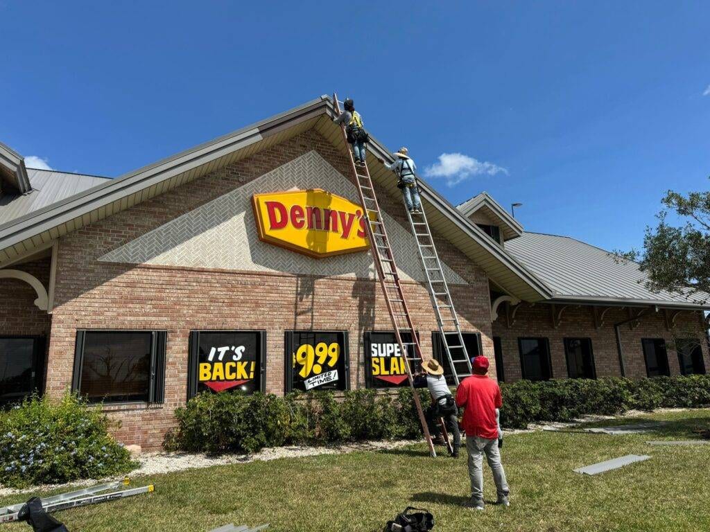 roofers on ladders on side of Denny's restaurant installing new commercial gutters