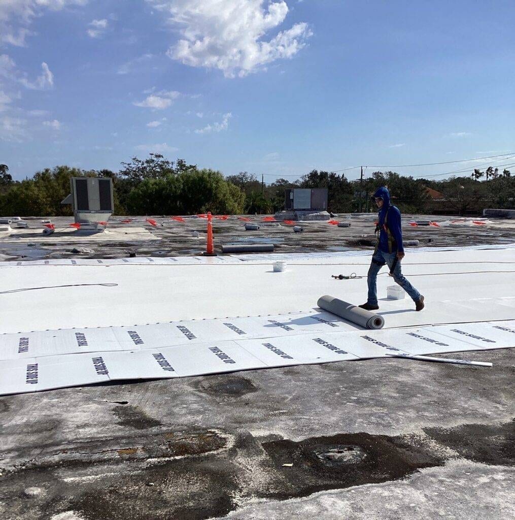 roofer rolling out single-ply roofing on a flat roof during replacement