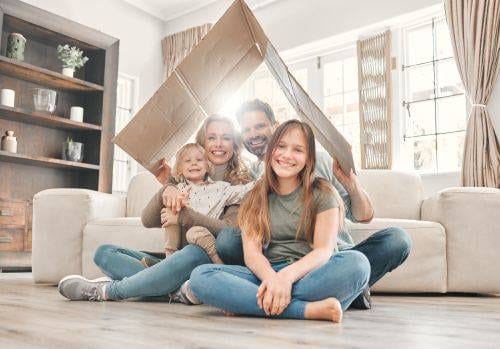 happy family smiling under cardboard box bent to be shaped like a roof