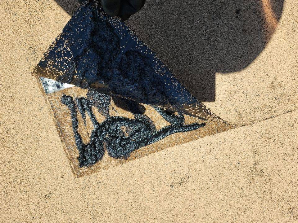 roofer lifting piece of asphalt roof showing black tar substance used as glue