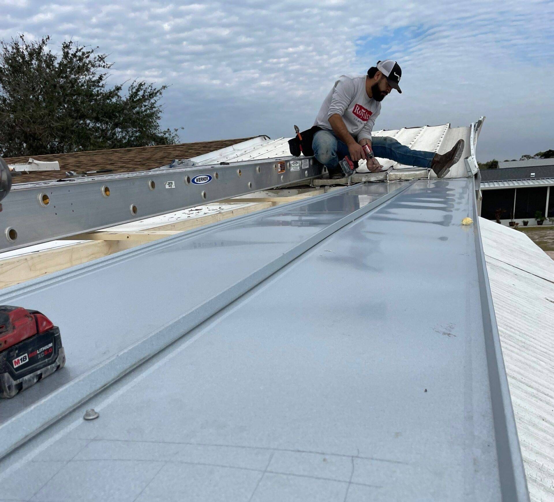 roof worker wearing royalty roofing shirt installing metal panels on a roof