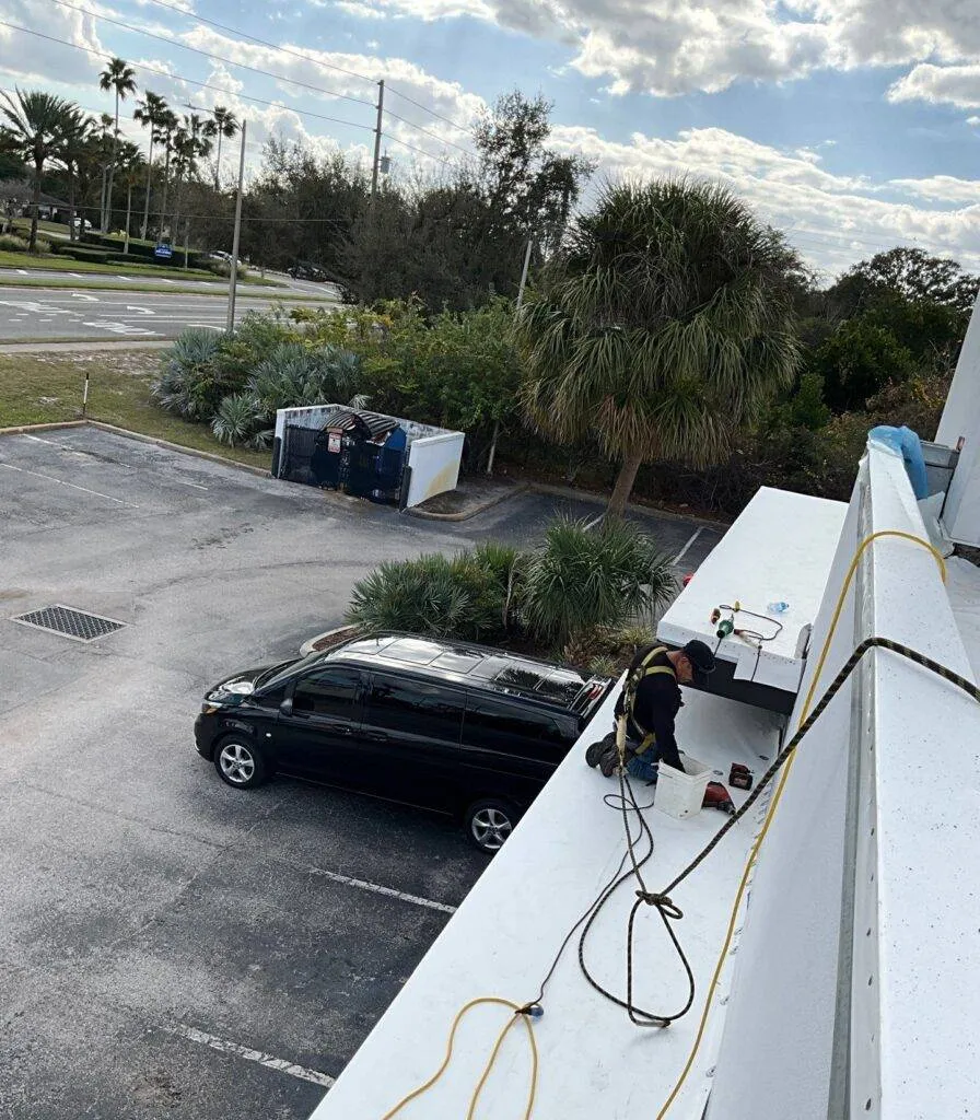 roofer wearing harness on awning of a flat roof working on roof replacement