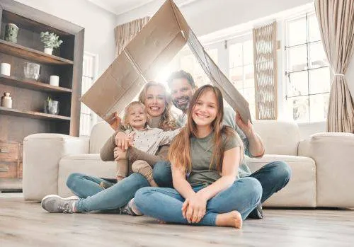 happy family smiling under cardboard box bent to be shaped like a roof