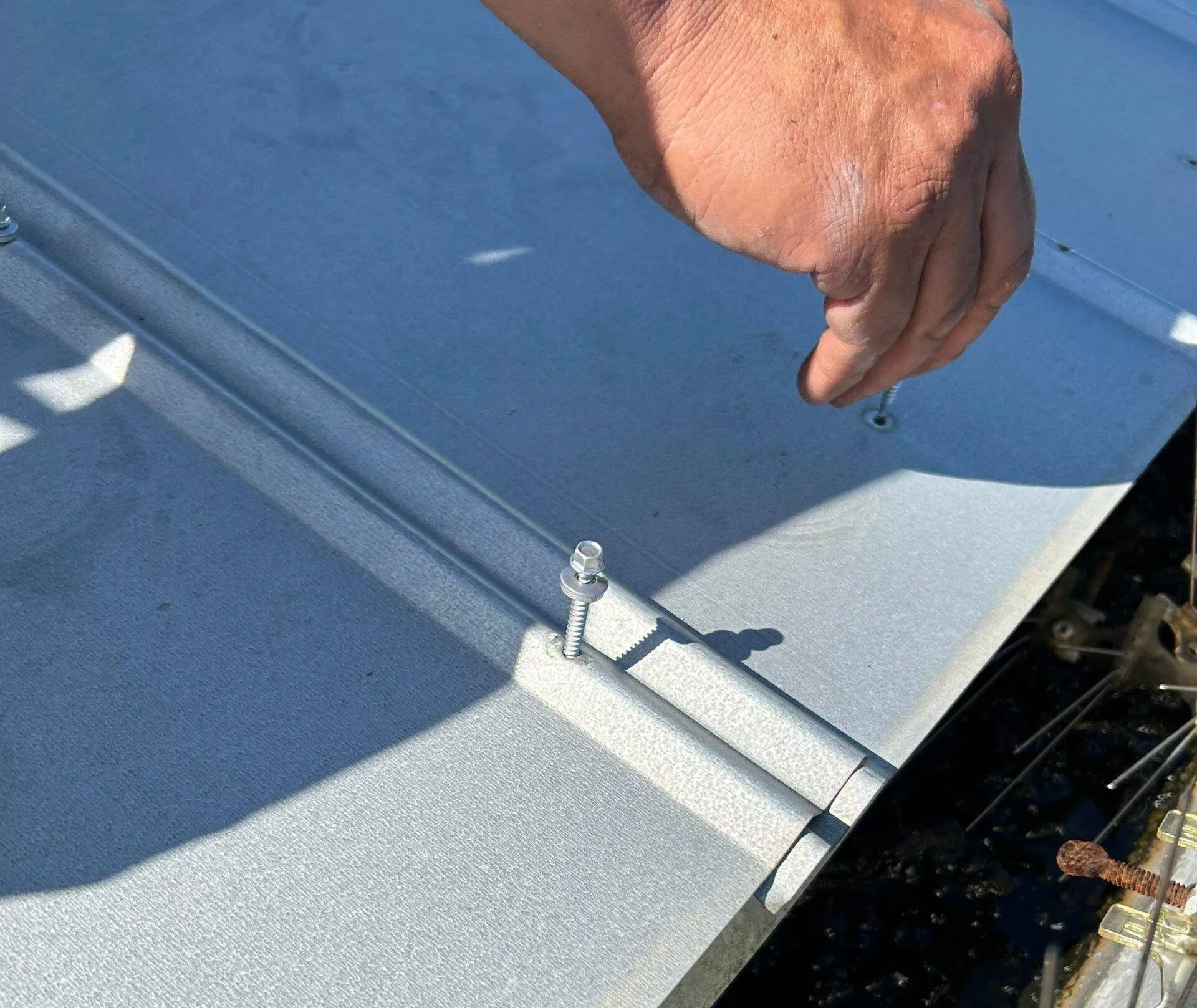 hand installing a fastener on a new standing seam metal roof panel on home